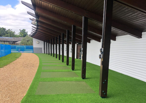 Covered outdoor tee line with light green synthetic grass boxes inside a dark green synthetic grass strip